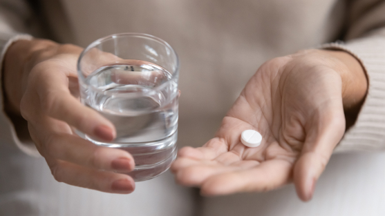 person holding glass of water and white pill in other palm